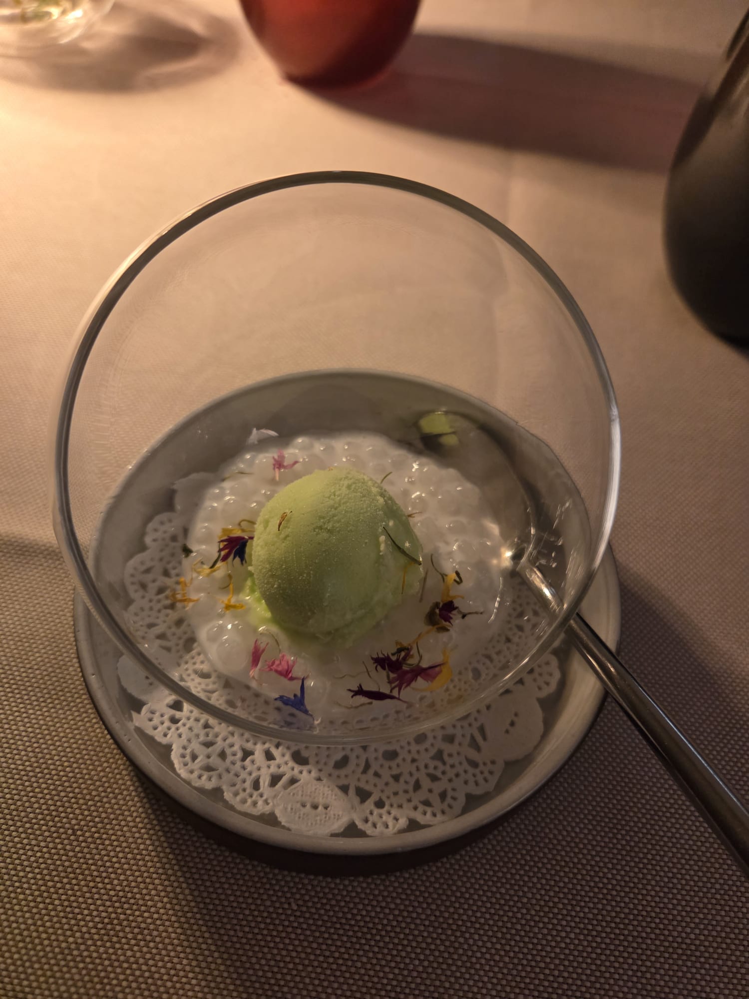 Coupe en verre ronde contenant du tapioca perlé, sorbet yuzu vert et fleurs, pré-dessert du Guillaume Tell